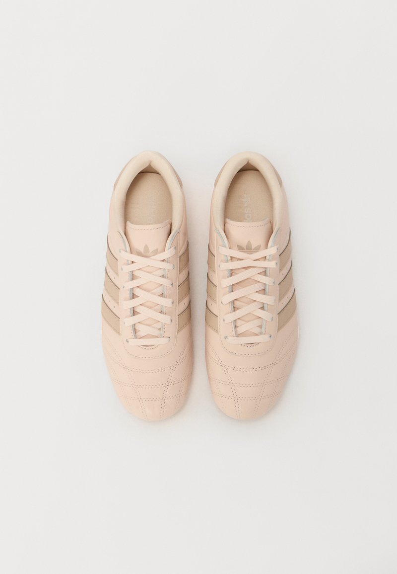 Zapatillas rosa claro con parte superior de cuero texturizado, que presentan tres rayas beige, cordones planos y punta redondeada.