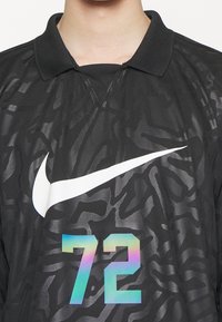 Maillot de sport noir avec un motif abstrait subtil, grand logo Nike blanc, et le numéro 72 irisé à l'avant, porté par une personne.