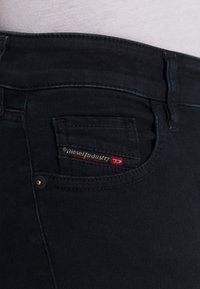 Svarta jeans i denim med en bakficka som har en röd och vit etikett "Diesel Industry" samt silverfärgade detaljer på framsidan.