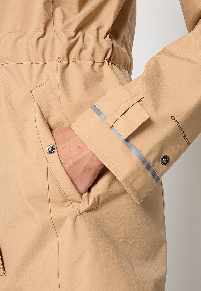 Giacca utilitaria beige con vita regolabile, tasca con bottone a scatto e polsini con striscia riflettente. Tessuto liscio e leggero.