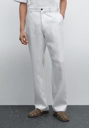 White linen trousers with a relaxed fit, featuring front pockets, a single black button, and paired with dark green sandals.