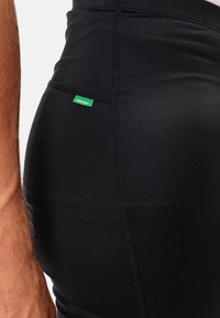 Fekete sportlegging sima textúrával, kontrasztos varrásokkal. Egy kis zöld címke látható, amely "Green Shape" felirattal van ellátva.