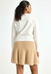 Beige fuzzy strikket nederdel med flaret kant sat sammen med en hvid fuzzy sweater med ribbet talje. Bagfra, der viser bløde teksturer.