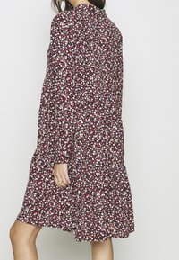 Květinové šaty v tmavě červené barvě s překládanou sukní. Obsahují malé, vícebarevné květiny, dlouhé rukávy a kulatý výstřih.