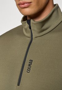 Pullover de cremallera en color verde oliva, fabricado en un tejido suave y mate, con una cremallera negra y el logo "COLMAR" impreso verticalmente en el pecho.