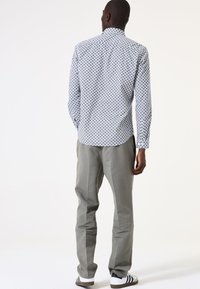 Camisa de botones blanca y azul con un cuello puntiagudo, combinada con pantalones grises claros y zapatillas de deporte en blanco y negro.