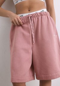 Shorts de sport en coton rose avec taille élastique, cordon de serrage et poches latérales ; logo imprimé sur la taille et à l'avant.