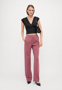Zwarte crop top met kapmouwen, gecombineerd met hoogzitende, roze wijde broek. Model houdt een kleine zwarte handtas vast en draagt puntige zwarte hakken.