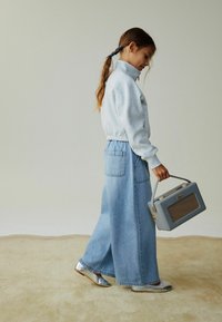 Sivi pulover s visokim ovratnikom, plave široke traperice, srebrne cipele i svijetloplawa torbica s mrežastim detaljem.