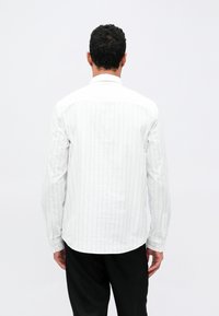 Hvit langermet skjorte med vertikale striper, knappede mansjetter og avrundet søm. Stoffet virker lett og strukturert, designet for uformelt bruk.