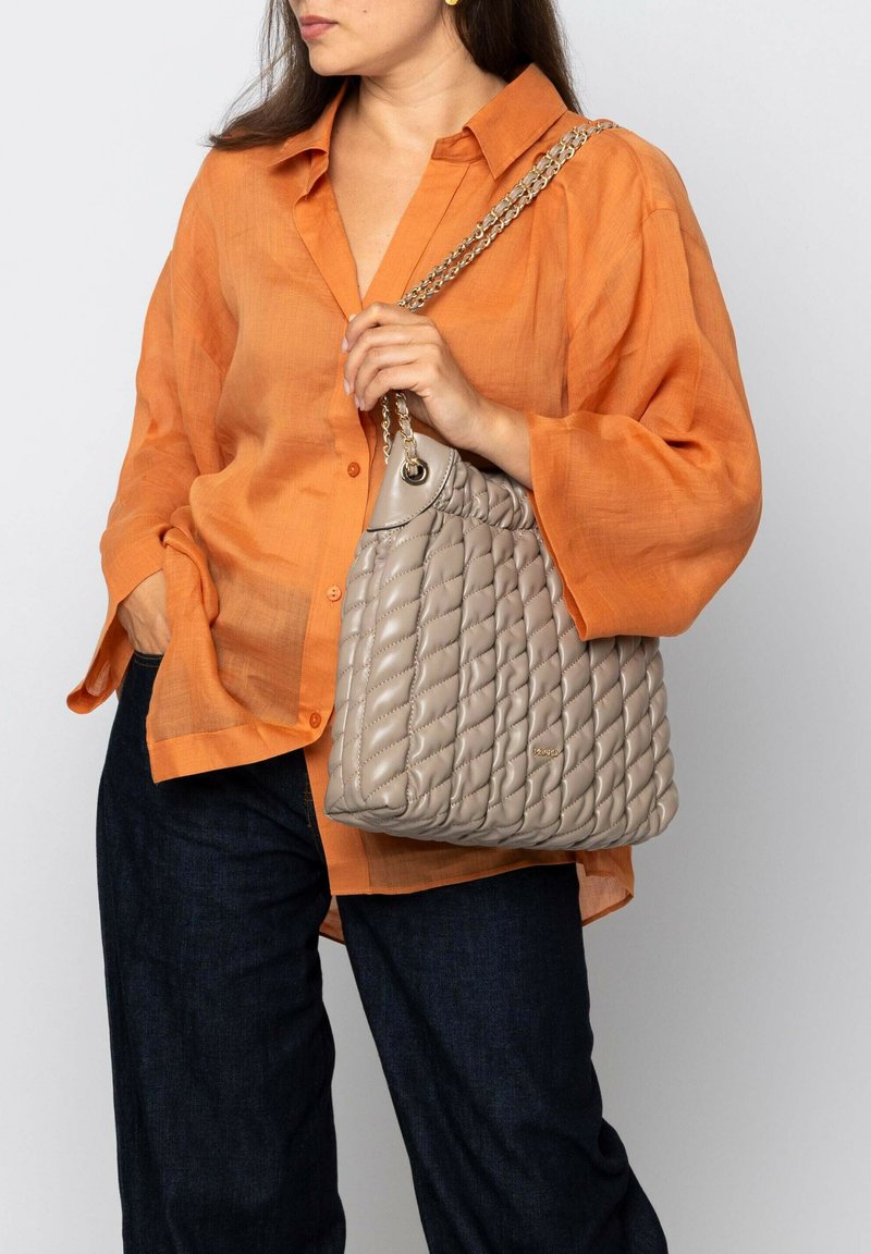 Sac à main matelassé beige avec une bandoulière en chaîne. Fabriqué en matériau doux, avec un dessus arrondi et un motif en diamant distinct. Couleur neutre.