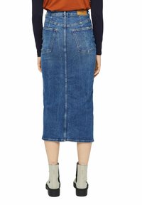 Džínová tužková sukně v středně modré barvě s vysokým pasem, zadními kapsami a přímým střihem. Nosit s béžovými kotníkovými botami.