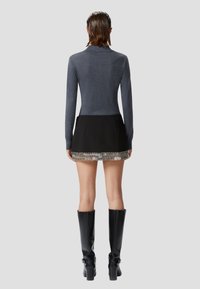 Maglia grigia a maniche lunghe, mini gonna nera con dettaglio in catena argentata all'orlo, abbinata a stivali neri con tacco alti fino al ginocchio.