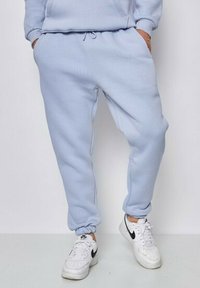 Pantalons de survêtement bleu clair en tissu doux, avec une taille élastique et des poignets, dotés de poches et d'une coupe décontractée. Associés à des baskets blanches.