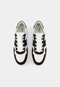 Sneakers med en kombination av svart mocka och vit läder, med vita snören, rund tå och en texturerad sula.