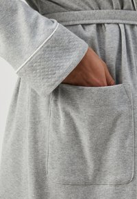 Robô de banho cinza com textura acolchoada nas mangas e um bolso frontal. Apresenta um cinto de laço e piping em contraste ao longo do colarinho.