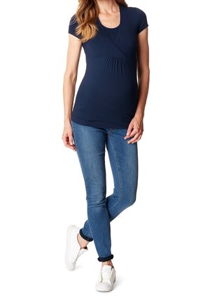 Tummansininen odotuspaidat, jossa on lyhyet hihat, kietaisumallinen muotoilu ja laskostettu yksityiskohta, yhdistettyinä tiukkoihin sinisiin farkkuihin ja valkoisiin tennareihin.