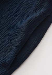 Tessuto navy testurizzato che mostra un motivo stropicciato, con una finitura morbida e bordi lisci. Il bordo piegato è leggermente visibile sul lato destro.
