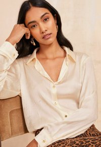 Bluză button-up texturată, de culoare crem, cu guler, având butoane aurii. Purtați-o cu o fustă cu imprimeu animalier.