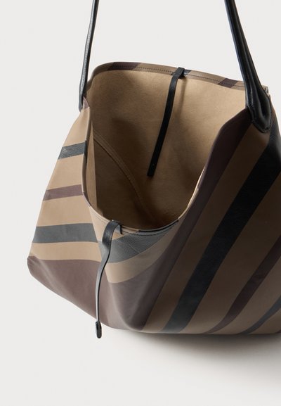 Sac cabas ouvert à rayures beiges et brunes, avec des poignées et des finitions en cuir noir, sur un fond uni et clair.