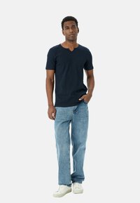 Marineblå V-hals kortærmet skjorte med struktureret stof, parret med lyseblå lige ben jeans og hvide sneakers.