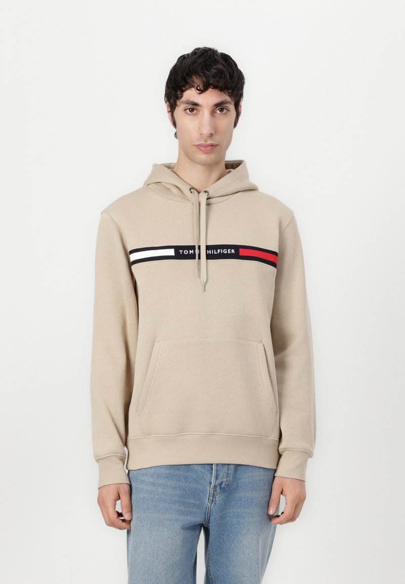Bežinė džinsinė su priekinėmis kišenėmis, su raišteliu, ir grafika, kurioje yra juodos, baltos ir raudonos juostelės su užrašu "TOMMY HILFIGER".
