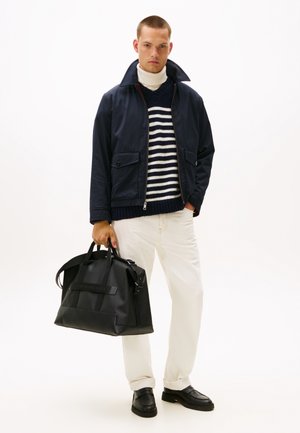 Giacca blu navy con ampio colletto, dolcevita crema, maglione a righe blu, pantaloni bianchi e borsa nera. Texture lisce, design minimal.