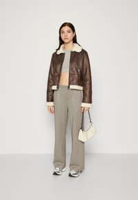 Giacca cropped in pelle marrone con colletto in shearling bianco, abbinata a pantaloni a gamba larga in tartan e una piccola borsa crema. In mostra scarpe da ginnastica argento.