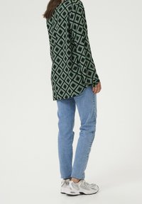 Camisa de manga larga en un patrón geométrico negro y verde, combinada con jeans de mezclilla azul claro y zapatillas deportivas grises. Corte relajado, dobladillo redondeado.