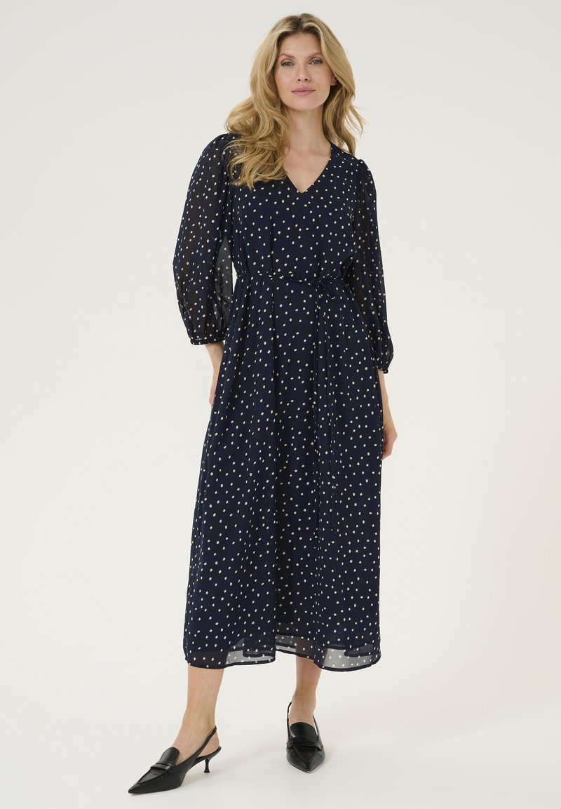 Marinblå klänning med polka prickar, V-ringning, långa genomskinliga ärmar, cinchad midja och längd till anklarna. Matchad med svarta spetsiga slingbacks.
