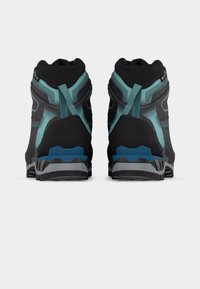 Ζευγάρι μαύρα και τιρκουάζ παπούτσια πεζοπορίας με θηλιές για kéo, παχιά πέλματα και ετικέτα GORE-TEX, εμφανιζόμενα από πίσω σε λευκό φόντο.
