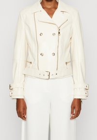 Veste de moto en cuir blanc avec un design double boutonnage, fermeture éclair sur le devant et taille ceinturée. Équipée de finitions en métal argenté et de poignets ajustables.