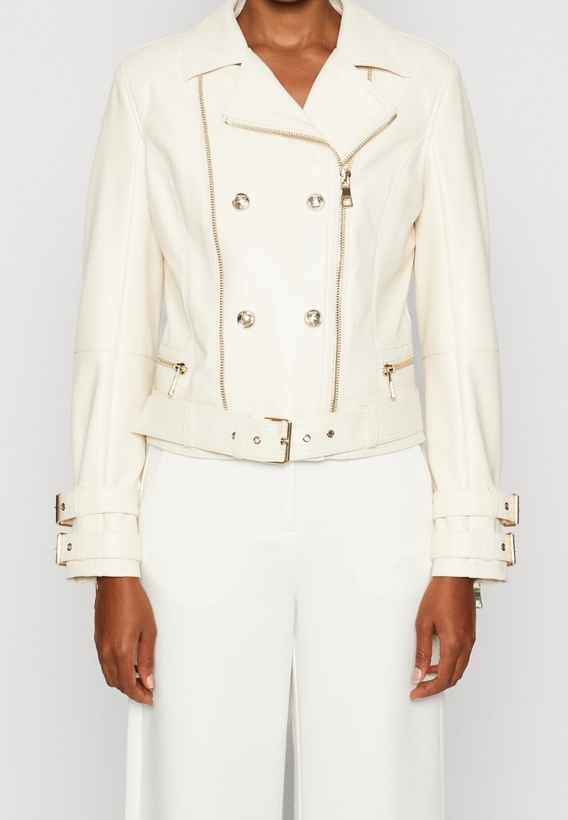 Veste de moto en cuir blanc avec un design double boutonnage, fermeture éclair sur le devant et taille ceinturée. Équipée de finitions en métal argenté et de poignets ajustables.