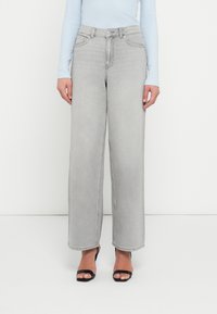 Γκρι τζιν παντελόνια με φαρδιά μπατζάκια και ψηλή μέση, με μπροστινές τσέπες και κλείσιμο με φερμουάρ. Συνδυασμένα με ανοιχτό μπλε τοπ και μαύρες πέδιλες με ανοιχτά δάχτυλα.