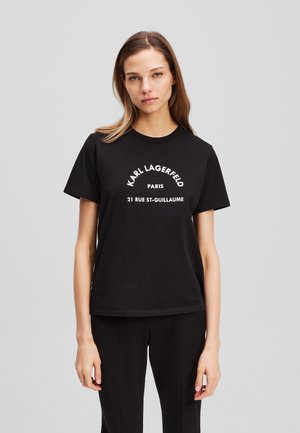 Musta puuvillapaita, jossa valkoiset tekstit: "KARL LAGERFELD PARIS 21 RUE ST-GUILLAUME." Pyöreä kaula-aukko, lyhyet hihat, rento malli.