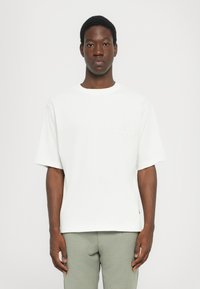 White short-sleeve T-shirt with a crew neck, featuring a subtle embossed "MK" logo on the chest and a relaxed fit.