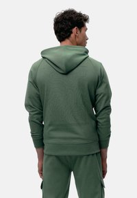 Grüne Kapuzenjacke mit strukturiertem Muster auf dem Rücken, ausgestattet mit einer Kordelzugkapuze, gerippten Bündchen und einer lockeren Passform. Passt zu passenden Hosen.