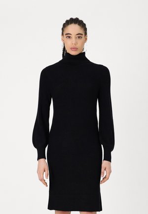Black knit dress featuring a high turtleneck, long puff sleeves, and a fitted silhouette that falls above the knee with side slits.