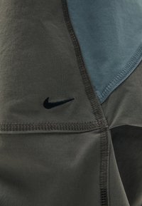 Športové oblečenie Nike s modro-sivým farebným blokovaním, zhotovené z ľahkej tkaniny s viditeľným švom a čiernym logom.