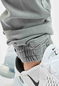 Pantalones de chándal grises con puños fruncidos combinados con zapatillas Nike blancas y negras, que presentan detalles de malla y textura a lo largo de los lados.