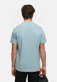 Ljusblå kortärmad t-shirt med rund hals, mjuk textur och en subtil söm detalj bak. Tillsammans med svarta byxor.