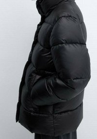 Schwarze Pufferjacke mit einer gesteppten Textur, ausgestattet mit einem Stehkragen, vorderen Knöpfen und seitlichen Taschen, in einer lockeren Passform geschnitten.