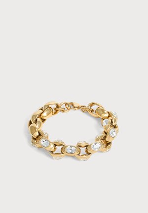 Bracelet chaîne en or avec de gros maillons, chaque maillon serti d'une pierre précieuse ovale claire, posé sur une surface claire et simple.