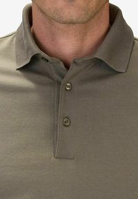 Oliivivihreä polo-paita pehmeällä tekstuurilla, lyhyellä kauluksella ja kolmella napilla. Siinä on suora helma ja minimaalinen ompelu.