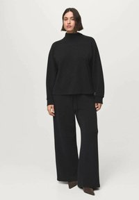 Pull en tricot noir avec col montant, manches larges et pantalon ample assorti. Le tissu semble doux avec une texture lisse.