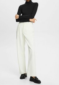 Svart långärmad polotröja i kombination med vita högmidjade vida byxor och svarta klackloafers.