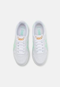White sneakers with mint green accents, perforated detailing, and a textured sole. Features white laces and an orange logo tab on the tongue.