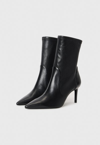 Zwarte leren enkelboots met eenpuntige neus en slanke hoge hak. Glad textuur, aansluitend ontwerp en gestikte details bij de rand.