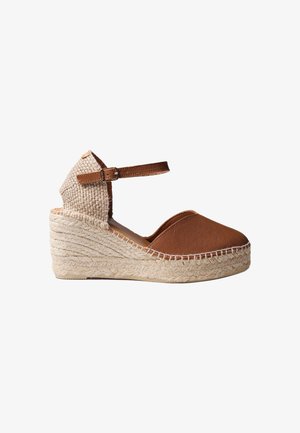 Espadrille à talon compensé marron avec talon tressé, bout fermé et bride ajustable à la cheville sur fond blanc.