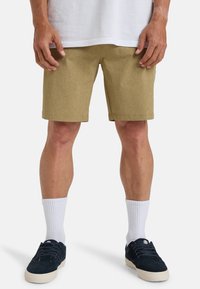 Tan shorts with a textured fabric, falling just above the knees, paired with white crew socks and dark sneakers. Casual fit and design.